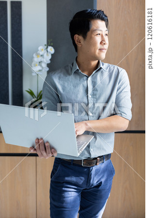 Holding laptop, asian man standing in office, looking out window, thinking 120616181