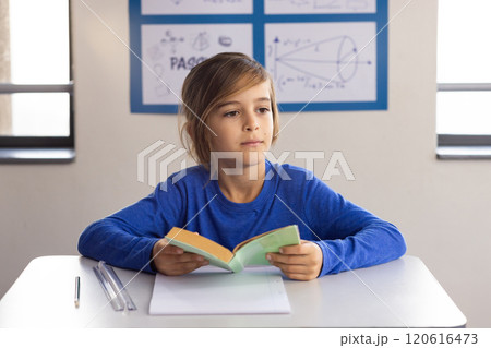 In school, boy reading book at desk with notepad and pens In school, boy reading book at desk with notepad and pens 120616473
