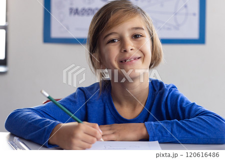 In school, smiling boy holding pencil and writing in classroom 120616486