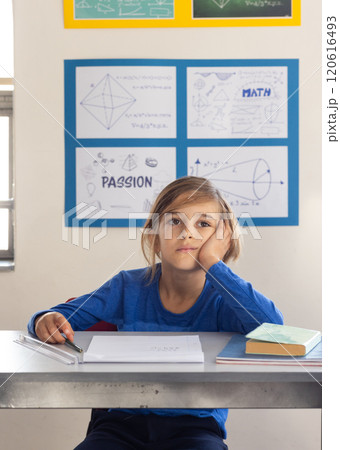 In school, boy sitting at desk daydreaming with books and papers In school, boy sitting at desk daydreaming with books and papers 120616493