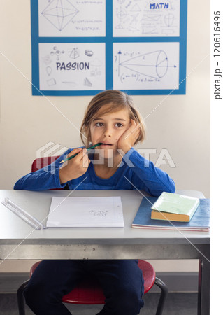 In school, boy sitting at desk thinking while holding pencil in classroom 120616496