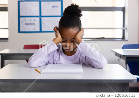 In school, african american girl sitting at desk with notebook and pencil, looking down In school, african american girl sitting at desk with notebook and pencil, looking down 120616513