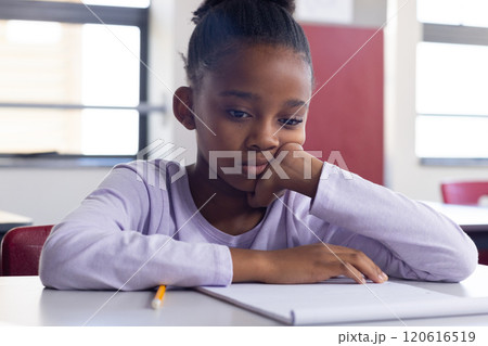 In school, african american girl sitting at desk looking at notebook, appearing thoughtful In school, african american girl sitting at desk looking at notebook, appearing thoughtful 120616519