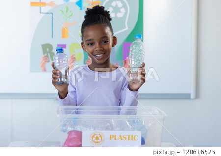 In school, african american girl holding plastic bottles and recycling in classroom 120616525