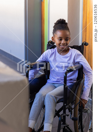 In school, african american girl in wheelchair smiling and looking ahead in hallway 120616536
