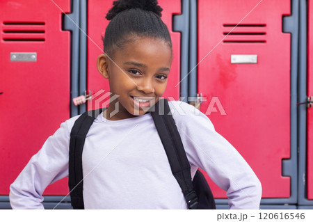 Smiling african american girl with backpack standing in front of red lockers at school Smiling african american girl with backpack standing in front of red lockers at school 120616546