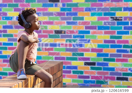 Listening to music with headphones, african american boy, brick wall outside school, copy space 120616599
