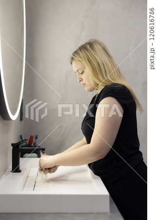 Blonde woman washing her hands at a modern sink in a minimalistic bathroom, focusing on hygiene and cleanliness. Blonde woman washing her hands at a modern sink in a minimalistic bathroom, focusing on hygiene and cleanliness. 120616786