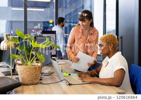 Collaborating at office, two women using laptop and documents discussing project Collaborating at office, two women using laptop and documents discussing project 120616864