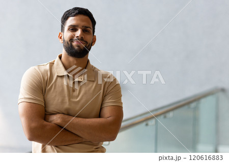 Confident man crossing arms and smiling, standing indoors near glass railing, copy space Confident man crossing arms and smiling, standing indoors near glass railing, copy space 120616883