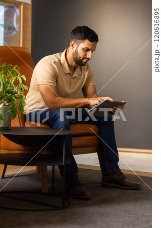 Using tablet, man sitting on chair and working in modern office 120616895