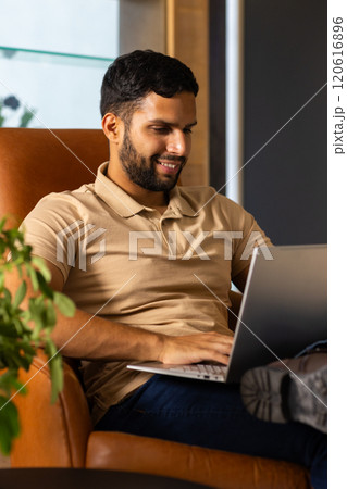 Smiling man using laptop while sitting on chair, working from home Smiling man using laptop while sitting on chair, working from home 120616896