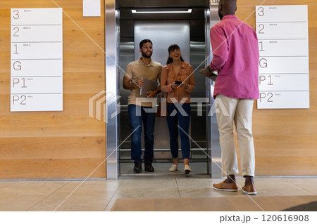 Exiting elevator, man and woman smiling and greeting colleague in office building Exiting elevator, man and woman smiling and greeting colleague in office building 120616908