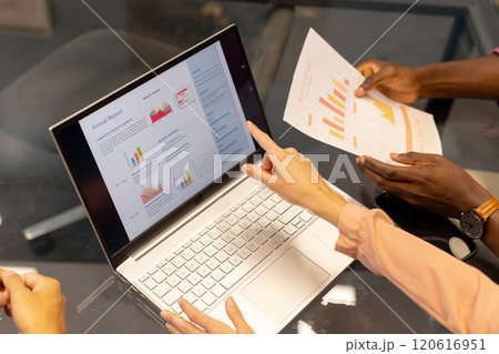 Pointing at laptop screen, colleagues in office discussing financial graphs and annual report 120616951