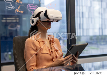 Using VR headset and holding tablet, woman working in modern office 120616958