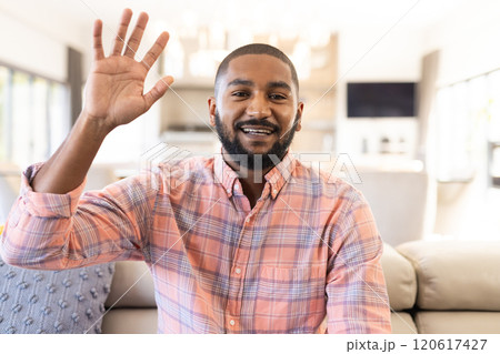 Smiling and waving hand, indian man greeting while sitting on sofa in living room, on video call Smiling and waving hand, indian man greeting while sitting on sofa in living room, on video call 120617427