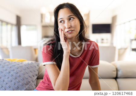 On video call, smiling woman in red shirt sitting on couch, at home On video call, smiling woman in red shirt sitting on couch, at home 120617468