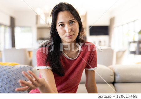On video call, Woman in casual red shirt gesturing while sitting on couch in living room, at home 120617469