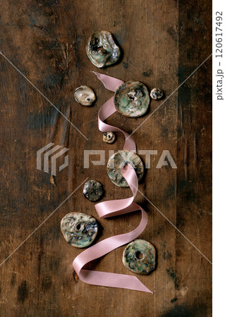Various handmade flat ceramic beads on pink ribbon. Hobby, jewelry assembly, DIY jewelry. Workshop idea. Dark wooden background, top view. 120617492