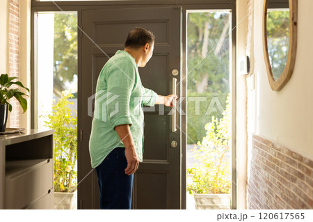 Opening front door, man in green shirt looking outside in bright daylight 120617565
