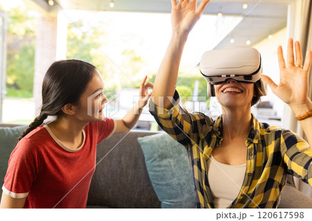 Using VR headset, mother enjoying virtual reality experience with daughter watching 120617598