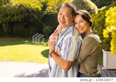 A couple, smiling middle-aged woman hugging asian man outdoors in sunny garden, enjoying family time A couple, smiling middle-aged woman hugging asian man outdoors in sunny garden, enjoying family time 120618077