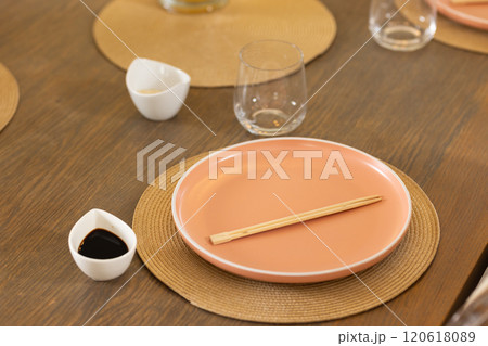 Chopsticks on pink plate with soy sauce and glass on dining table 120618089