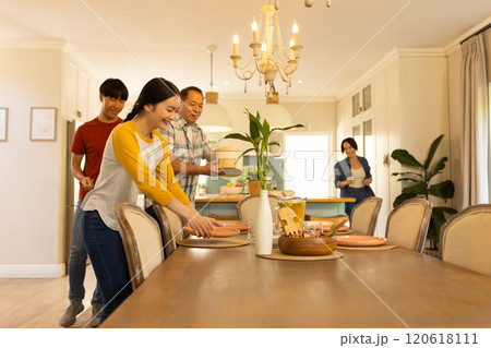 Setting dining table, multiracial family preparing for meal together in cozy home dining room 120618111