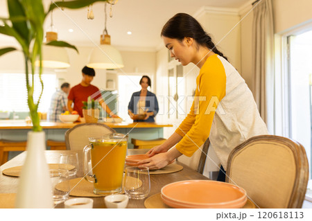 Setting table with plates and glasses, young asian woman preparing family meal in kitchen Setting table with plates and glasses, young asian woman preparing family meal in kitchen 120618113