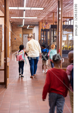 Walking in school hallway, female teacher guiding young diverse students with backpacks 120618390