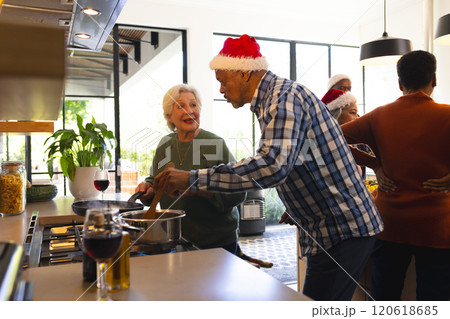 Happy diverse friends couple in santa hat preparing food in sunny kitchen at home Happy diverse friends couple in santa hat preparing food in sunny kitchen at home 120618685