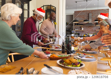 Happy diverse group of senior friends in santa hats serving food in sunny dining room at home 120618708