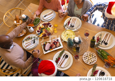 Diverse group of senior friends saying grace at christmas dinner in sunny dining room at home 120618718