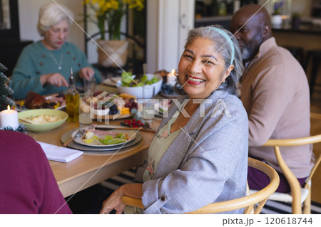 Happy biracial senior woman celebrating with friends at christmas dinner in sunny dining room 120618744