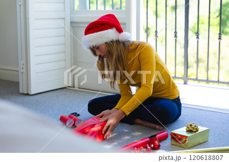 Happy caucasian woman in santa hat sitting on floor and packing gifts at christmas at home Happy caucasian woman in santa hat sitting on floor and packing gifts at christmas at home 120618807