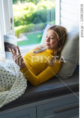 Happy caucasian woman lying on couch, reading book and smiling in sunny room at home Happy caucasian woman lying on couch, reading book and smiling in sunny room at home 120618816