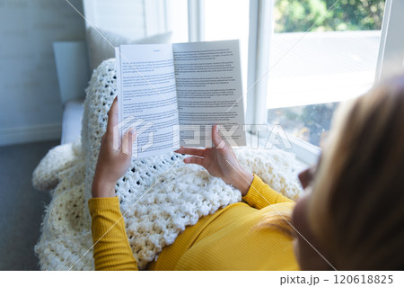 Caucasian woman lying on couch, reading book in sunny room at home 120618825