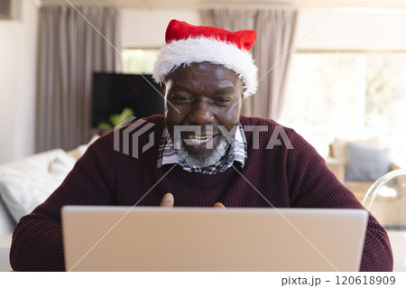 Happy african american senior man in christmas hat having laptop video call at home Happy african american senior man in christmas hat having laptop video call at home 120618909