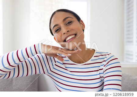 Portrait of happy biracial woman with striped blouse sitting on couch at home 120618959
