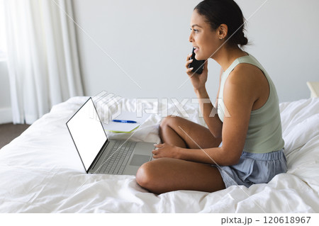 Happy biracial woman talking on smartphone with notebook and laptop with copy space at home Happy biracial woman talking on smartphone with notebook and laptop with copy space at home 120618967