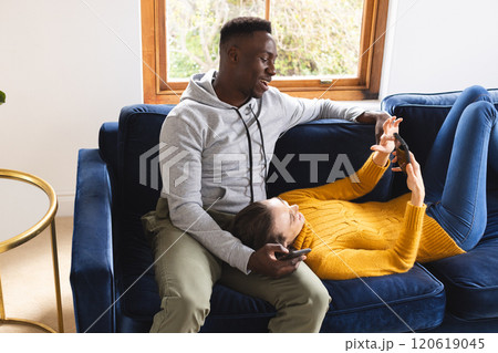 Happy diverse couple sitting on sofa using smartphones at home Happy diverse couple sitting on sofa using smartphones at home 120619045