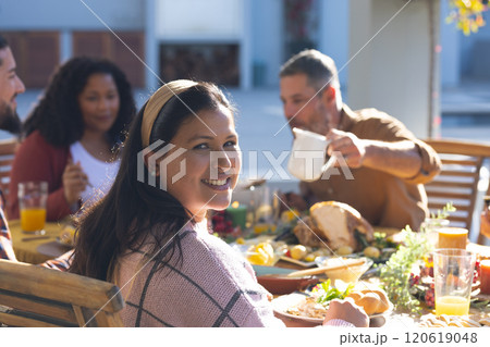 Happy biracial woman sitting with friends during thanksgiving celebration meal in sunny garden Happy biracial woman sitting with friends during thanksgiving celebration meal in sunny garden 120619048