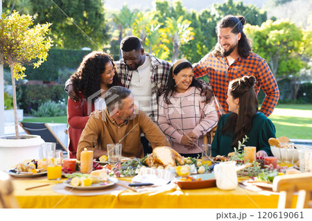 Happy diverse male and female friends posing during thanksgiving celebration meal in sunny garden Happy diverse male and female friends posing during thanksgiving celebration meal in sunny garden 120619061