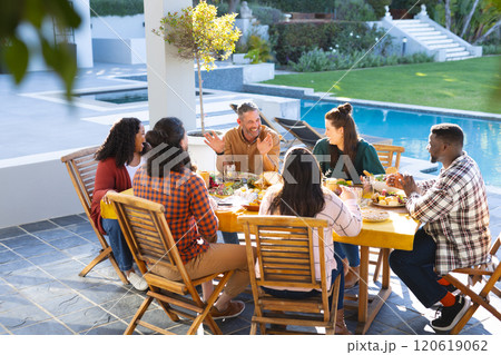 Happy diverse male and female friends eating thanksgiving celebration meal in sunny garden Happy diverse male and female friends eating thanksgiving celebration meal in sunny garden 120619062
