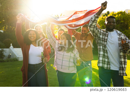 Happy diverse male and female friends holding american flag in sunny garden Happy diverse male and female friends holding american flag in sunny garden 120619083