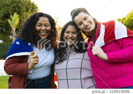 Three happy diverse female friends with flag on backs in sunny garden Three happy diverse female friends with flag on backs in sunny garden 120619086