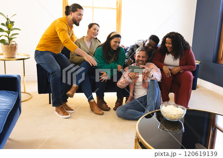 Happy diverse male and female friends relaxing at home together talking and looking at smartphone Happy diverse male and female friends relaxing at home together talking and looking at smartphone 120619139