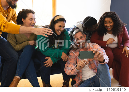 Happy diverse male and female friends relaxing at home together talking and looking at smartphone Happy diverse male and female friends relaxing at home together talking and looking at smartphone 120619140
