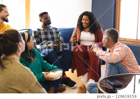 Happy diverse male and female friends talking, eating popcorn and drinking beer at home 120619159