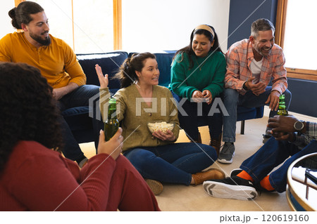 Happy diverse male and female friends talking, eating popcorn and drinking beer at home 120619160